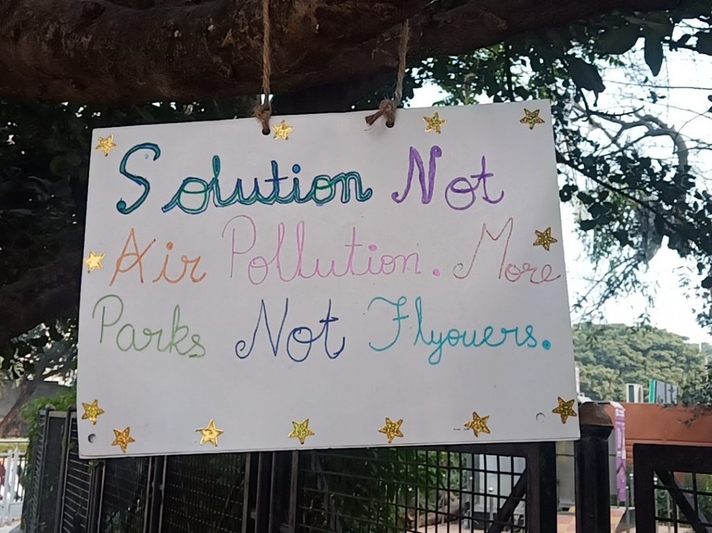 A sign that reads Solution Not Air Pollution. More Parks Not Flyovers. 