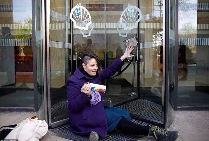 An activists sits blocking the entrance to Shell's headquarters, glued to the glass revolving door. 