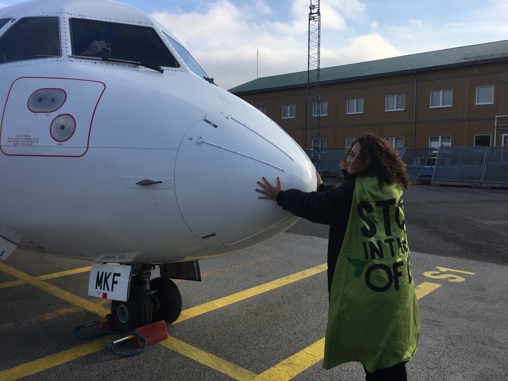 An XR activists stands, glued to the nose of a plane. 