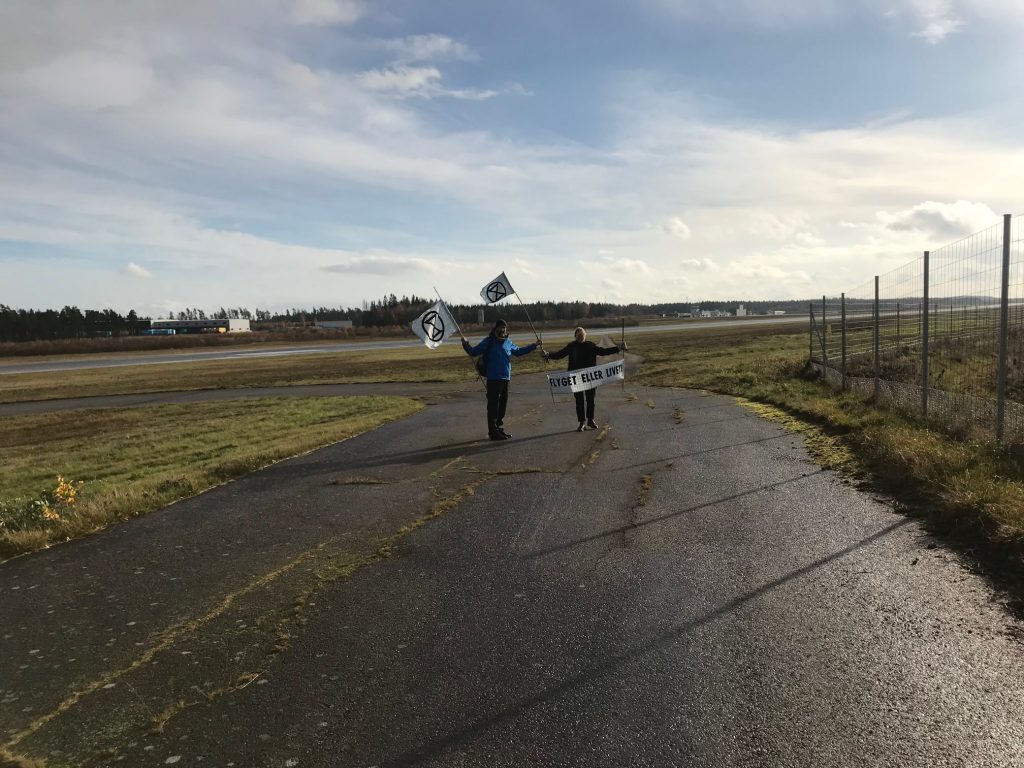 Two XR activists stand on a runway with flags. 